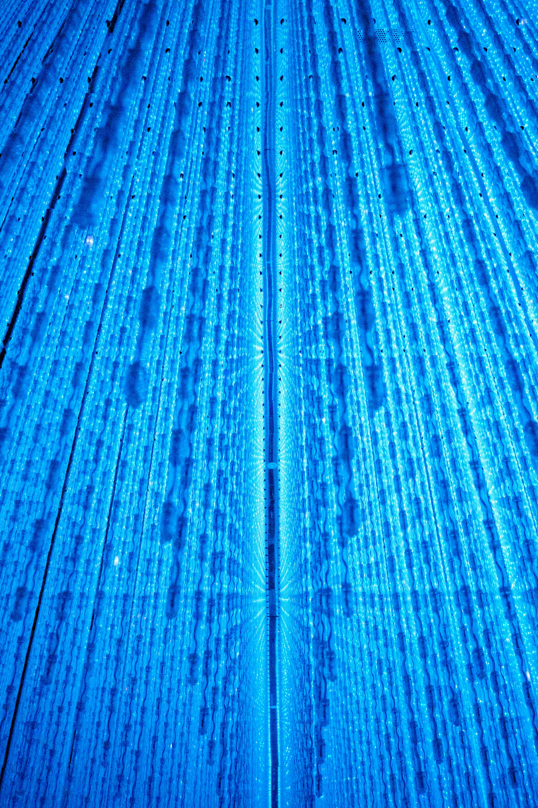 Instalação artística de luz com feixes azuis convergindo para ponto de fuga — metáfora visual de recursão e auto-referência